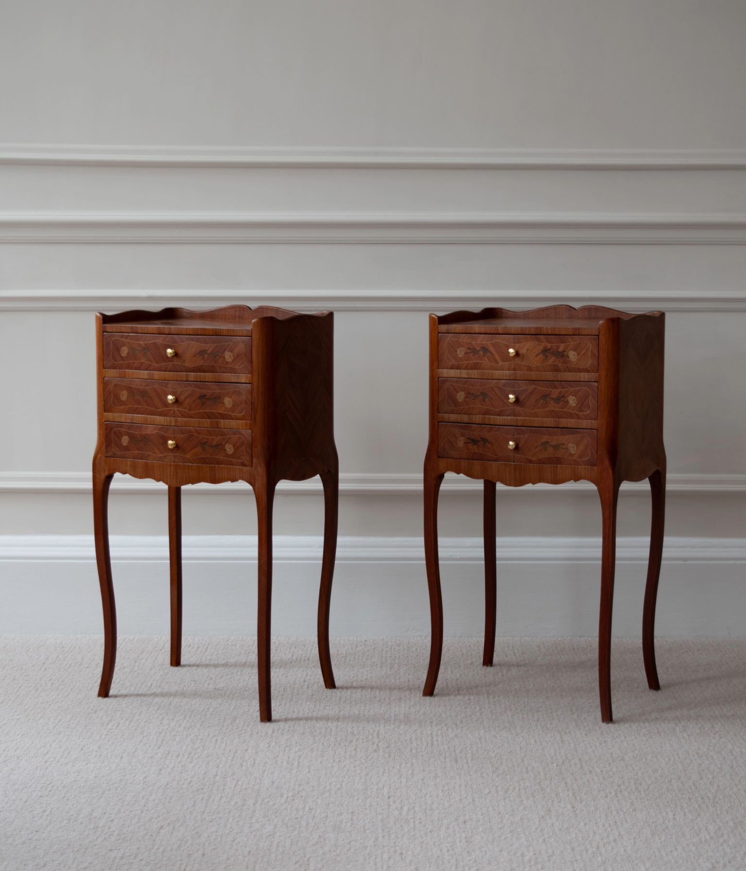 A pair of Louis XV-style antique bedside tables with marquetry inlay work, featuring tulipwood background and floral motifs, with brass handles and curved cabriole legs.