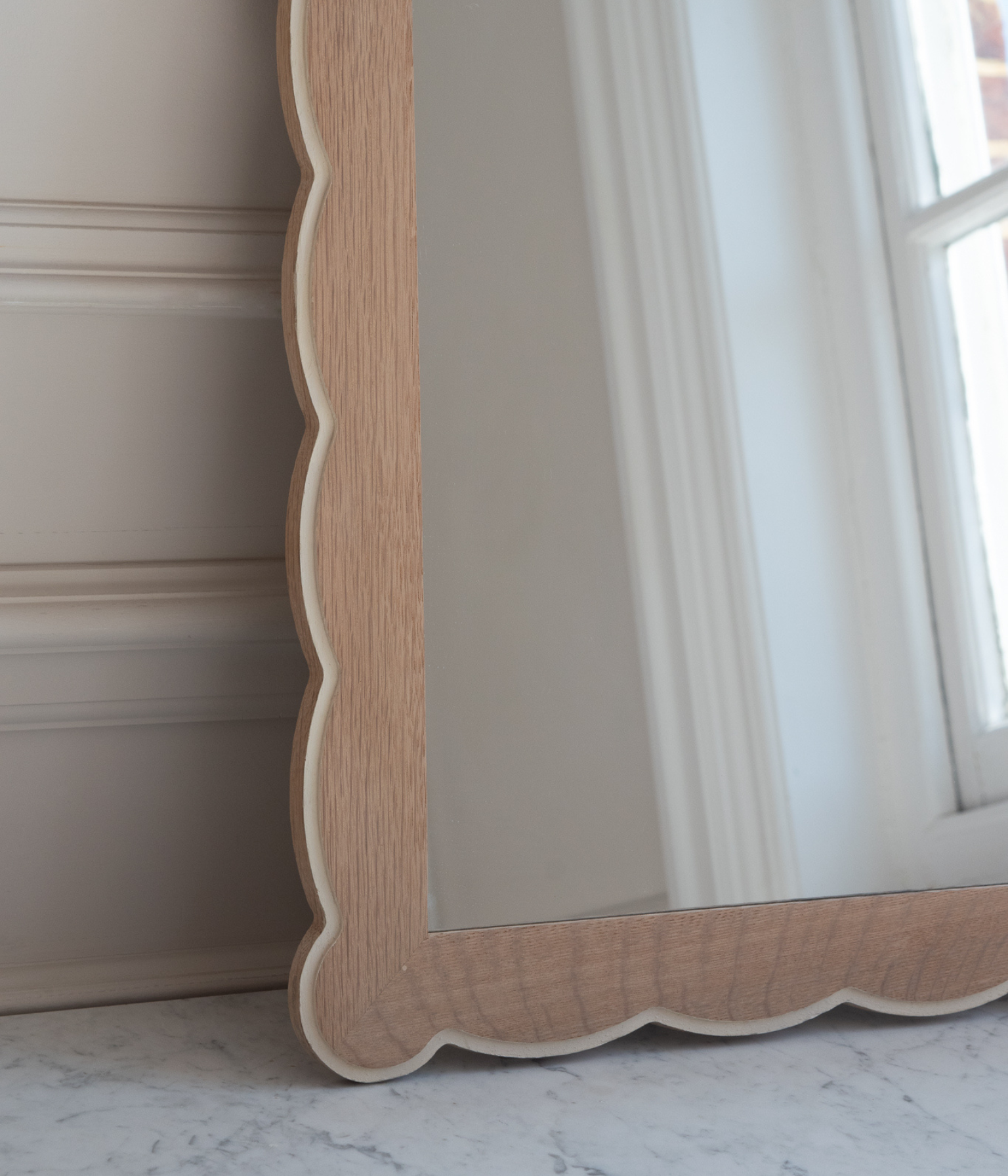Wooden-framed mirror with scalloped edge on a neutral background